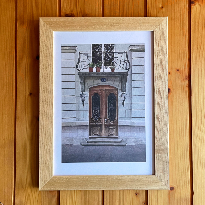 A wooden wall featuring a print of a door with ornate iron balcony. A watercolour painting by Rebecca Tinguely