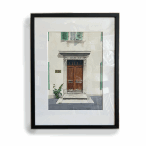 Peinture à l'aquarelle d'une porte en bois à La Chaux-de-Fonds, entre des murs blanches, avec des plants dans l'avant plan. Encadré en noir.